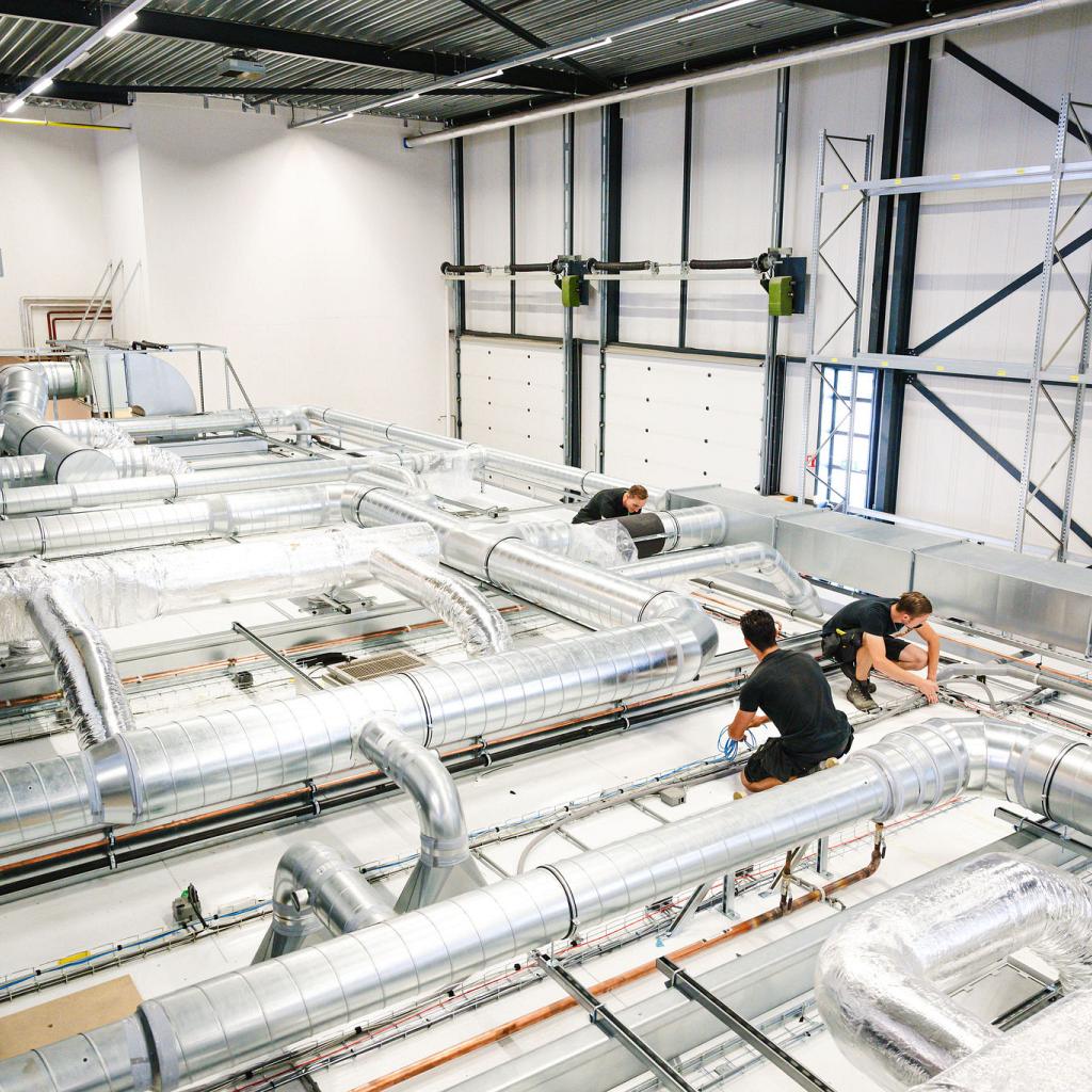 3 mannen aan het werk in een grote lichte bedrijfshal tussen alle buizen.